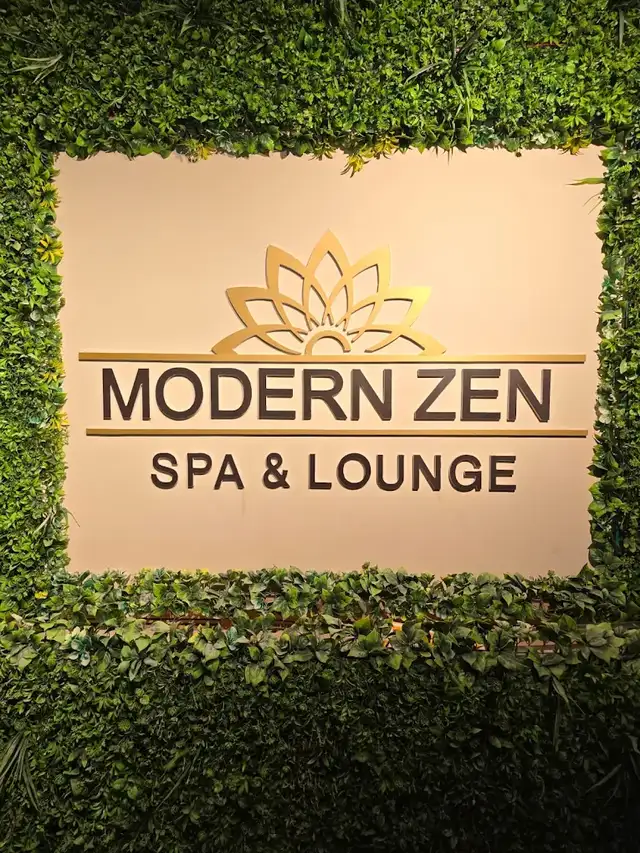 Brass lotus emblem and Modern Zen Spa & Lounge lettering mounted on a wall of green foliage